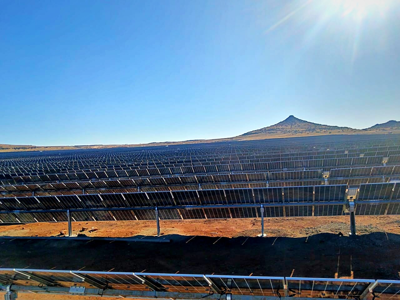 Rows of single-axis trackers and modules at Mooiplaats with a hill in the background