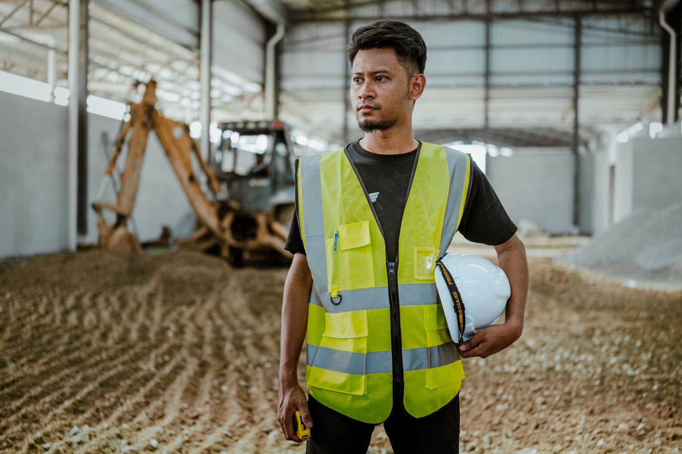Worker in a hi-vis vest and hard hat holding a helmet on an industrial site